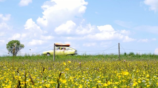 oldtimer with the boat on the roof goes on the sea through the meadow with flowers