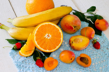 Fresh apricots, oranges and bananas on a white wooden table