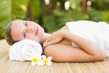 Obraz na płótnie Canvas Peaceful blonde lying on bamboo mat with flowers 