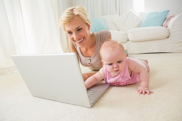 Happy blonde mother with her baby girl using laptop