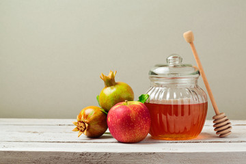 Honey jar, red apples and pomegranate on white wooden board