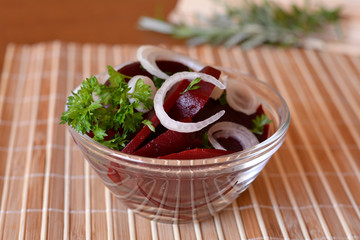 Fresh sliced beetroot salad with onion and parsley on a glass bowl on a table