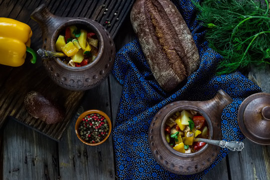 Ceramic pots with meat and vegetables on wooden background.