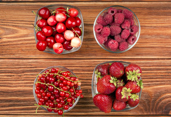 Strawberries, raspberries, currants and cherries in the cups on the wooden background.
