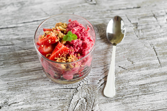 frozen yogurt with strawberries and cookie crumbs in a glass bowl on a light wooden background