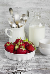 fresh strawberries in a white bowl and a bottle of milk on white wooden background
