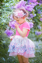 Fototapeta premium Little beautiful girl standing in the lilac park on a sunny morning and smiling.