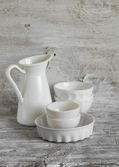 white vintage crockery - enamelled jug, ceramic bowl and baking dish on a light wooden background