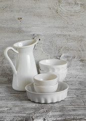 Fototapeta na wymiar white vintage crockery - enamelled jug, ceramic bowl and baking dish on a light wooden background