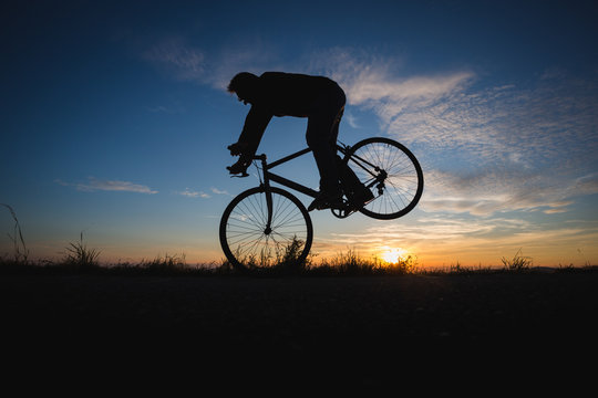 cyclist doing nose wheelie with race bike in sunset