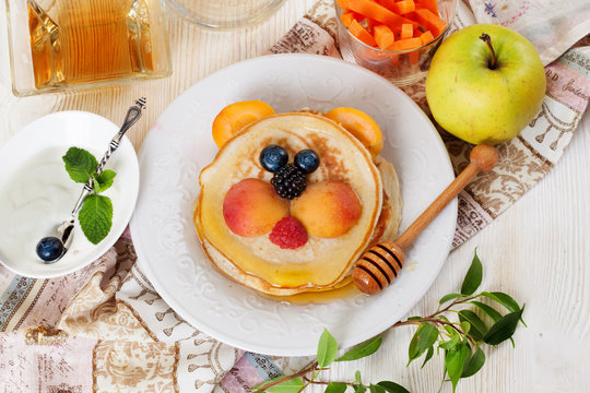 Children's breakfast pancakes smiling face of the baby teddy bear strawberry blueberry and apricot, cute food, honey