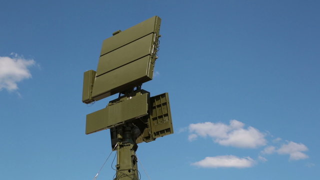 The rotating antenna of the radar on the background of blue sky with white clouds