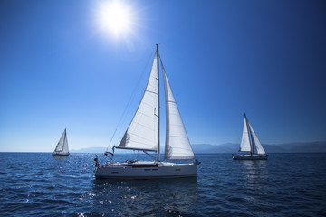Sailing ship yachts with white sails in the open Sea. Noon, the blue sky and the Sun at the Zenith.
