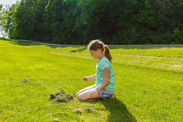 Little girl sitting and looking down on green grass field in outdoor park