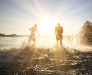 Glückliche junge Menschen laufen und springen am See beim Sonnenuntergang
