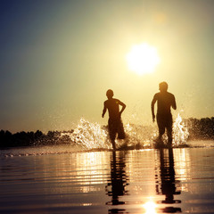 Glückliche junge Menschen laufen und springen am See beim Sonnenuntergang