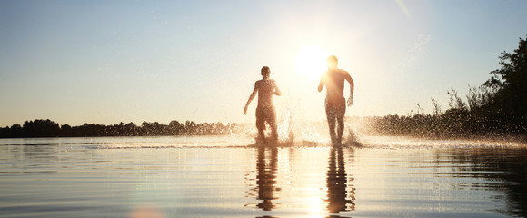 Glückliche junge Menschen laufen und springen am See beim Sonnenuntergang © Thaut Images