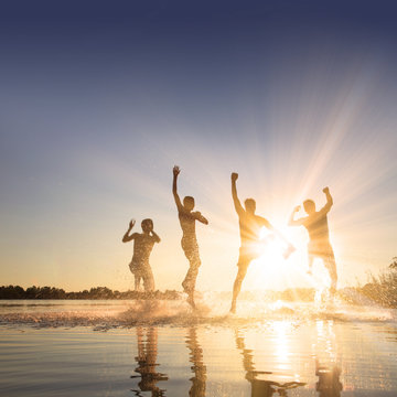 Gl&uuml;ckliche junge Menschen laufen und springen am See beim Sonnenuntergang