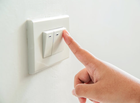 Womans hand with finger on light switch to turn off the lights.
