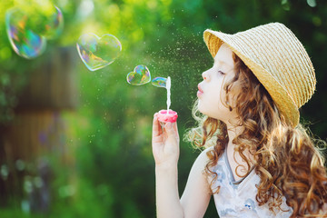 Little girl blowing soap bubbles in a heart shape. Happy childho