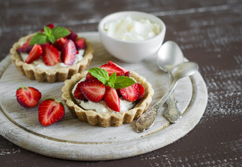 tartlets with cream and strawberries, decorated with mint leaves on wooden surface