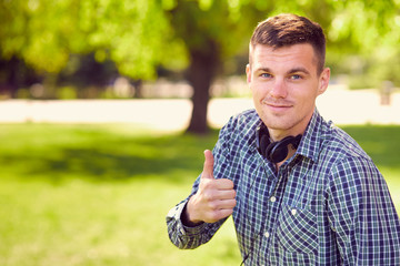 Naklejka na ściany i meble Smiling young man in a shirt with earphones shows a thumb in par