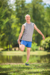 Joyful senior stretching his legs in a park