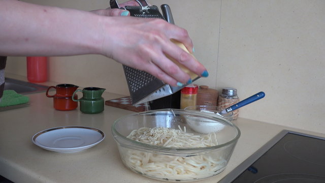 woman hand grated cheese on pasta spaghetti in kitchen. Dinner preparation. Static tripod shot. 4K UHD video clip.