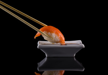 Salmon sushi nigiri in chopsticks with soy sauce over black background