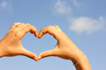 Female hands making the heart on the sky background