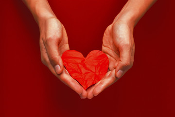 Obraz premium Crumpled red paper heart in hands on the red background