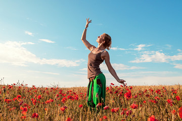 Young beautiful woman walking and dancing through a poppy field