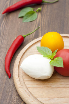 Mozzarella with herbs, fresh vegetables, chilli, on a wooden round board, selective focus