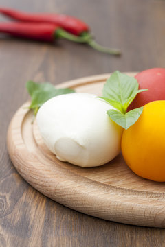 Mozzarella with herbs, fresh vegetables, chilli on a wooden round board, selective focus