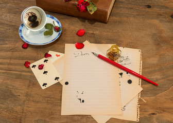   Tazzina  vuota con fondo di caffè in forma di cuore,carte da gioco,petali di rosa secchi e penna su fogli di quaderno.
