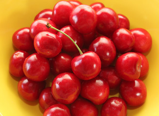 Ripe juicy cherries in a yellow plate close-up