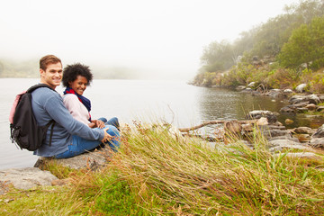 Naklejka na ściany i meble Hiking couple relaxing by the edge of a lake, looking to camera