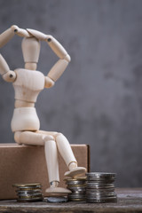 Small wooden dummy with sitting with coins over the grey concrete wall