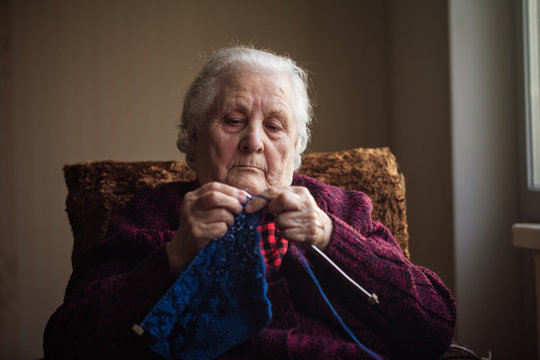 The old woman sits at home and knits garments.