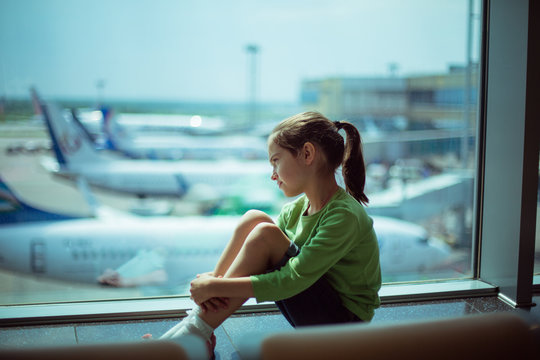 Child at the airport near the window looking at airplanes and waiting for time of flight.
