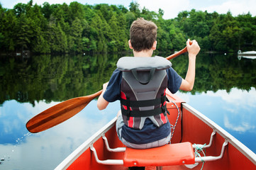 child in the front of a canoe paddling on a calm Canadian lake