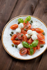 Caprese salad with capers, dark brown wooden background