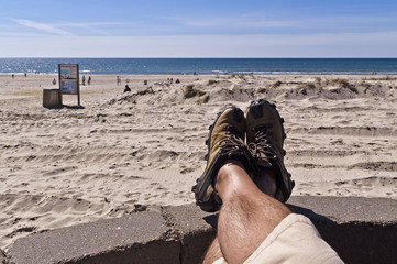 Mann liegt entspannt mit den Füßen uaf einer Terrassenbegrenzungsmauer und schaut über den Strand zum Meer