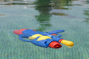 Colorful squirt gun floating in a swimming pool with green tiles floor