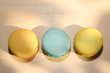 Traditional french yellow and blue macarons with sun shadows on wooden background