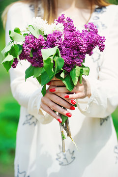 Woman hands with red manicure holding delicate spring lilac flowers bouquet