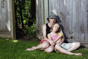 Mother and daughter sitting together outside leaning against a f