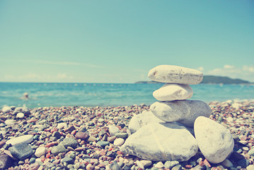 Stack of white stones balancing on the pebbly beach, on a sunny day. Image filtered in faded, washed out, retro style; summer vintage concept. Concept of balance, harmony and well-being. - 86156252