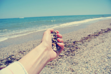 Female hand holding pebbles on the beach, on a sunny summer day. Image filtered in faded, washed out, retro style. Concept of adventure, travel, independence and freedom. Personal angle shot.