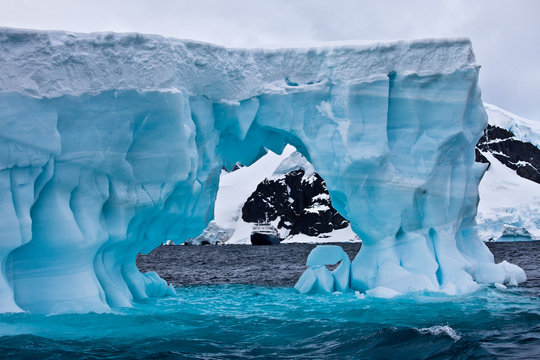 Huge blue iceberg with cruise ship in the distance, Antarctica